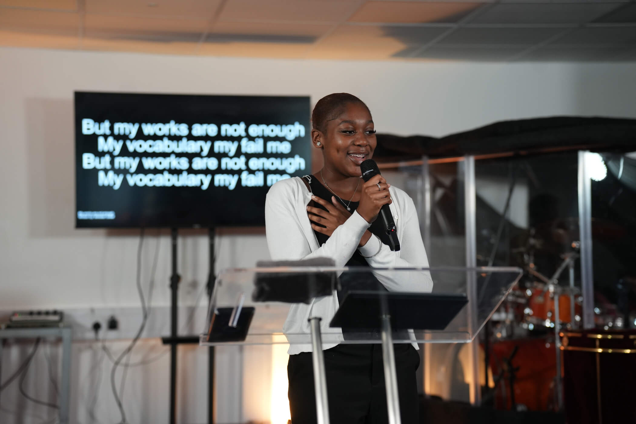 A young woman worshipping at the lectern with song lyrics on the screen behind her